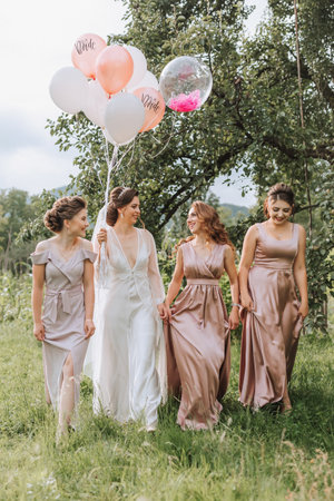 The bridesmaids look at the smiling bride. The bride and her fun friends celebrate a bachelorette party outdoors in matching dresses. The bride and friends on the grass under the open skyの写真素材