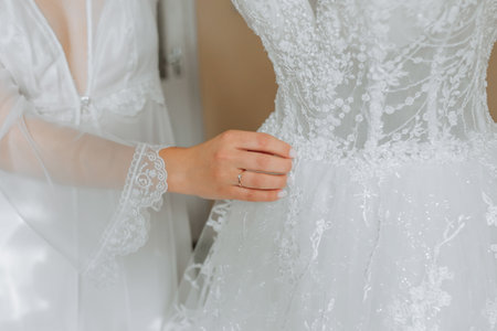 white wedding dress on a mannequin in the room, close-up of the bride's hand on the mannequin. Wedding details, modern wedding dress with long train, long sleeves and open backの写真素材