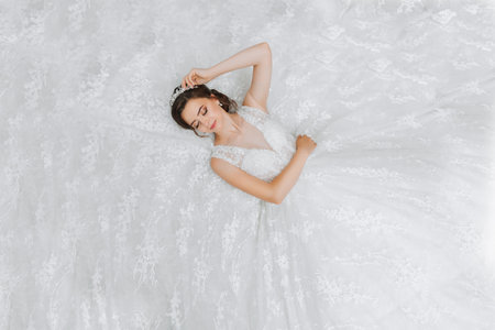 young beautiful bride in wedding dress, lying down, fashion shot under studio light. The photo is taken from aboveの写真素材