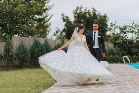 Portrait of the bride and groom. Bride and groom dancing by the pool, holding hands. Wedding walk near the hotel. Long train of the dressの写真素材