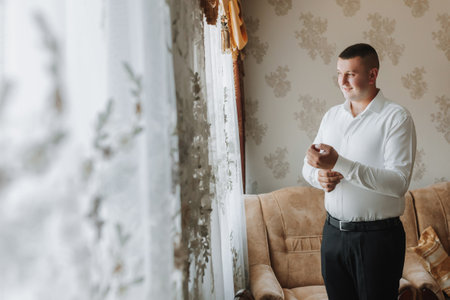 the man fastens the buttons on his shirt sleeve. The groom is preparing for the wedding.の写真素材