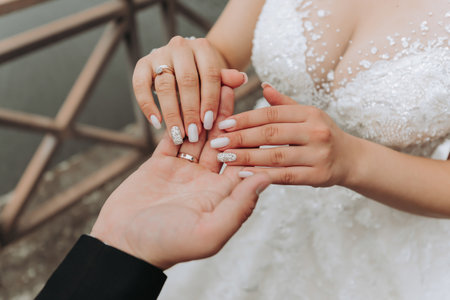 The groom gently holds the bride's hand against the background of the lake. Gentle manicure. Beautiful hands. Jewelry on the hand. Close-up photoの写真素材