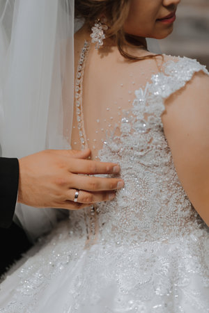 Wedding portrait. The bride in an elegant dress stands in front of the groom in a classic suit, against the background of green trees. Gentle touch. Summer wedding. A walk in natureの写真素材