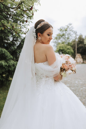 Rear view portrait of beautiful bride in white wedding dress with long train with modern hairstyle and veil walking in the garden. Wedding conceptの写真素材