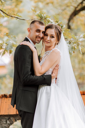 Fashionable groom and cute brunette bride in white dress with professional make-up and bouquet of...