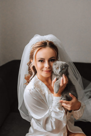 a young, elegant girl in the image of a bride with a beautiful veil on her head, holding her domestic cat in her arms Scottish Foldの写真素材