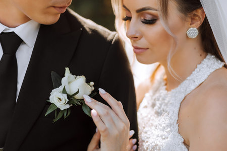 A stylish groom in a black suit and a cute bride in a white dress with a long veil are hugging in a park near an old house. Wedding portrait of smiling and happy newlyweds.の写真素材