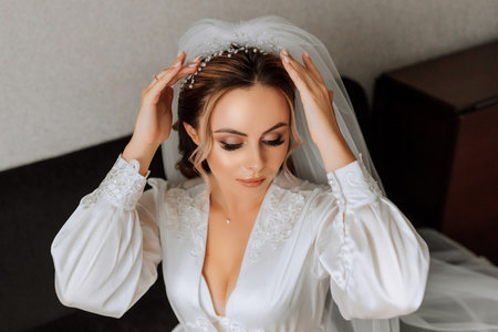 the bride in a white satin gown, professional hair and makeup, and a long veil. the morning before the wedding.の写真素材
