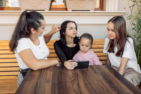 teenagers and one child having fun outdoors in a cafe. Friendship of children and teenagers. Four girls, dressed in different clothes, shout on the phoneの写真素材