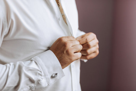 Close-up of a man buttoning his shirt. The groom is preparing for the wedding. The man wears a white shirt. Stylish groomの写真素材