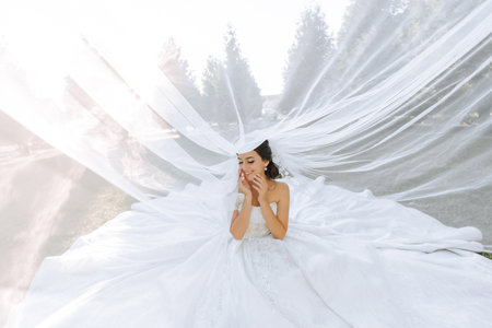 tender portrait of a happy bride with a bouquet of orchids in her hands, outdoors. Warm summer time. A long veil, a luxurious white dress with a train.の写真素材
