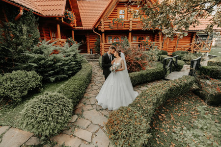 gorgeous elegant luxurious bride with veil blowing in the wind. and a stylish groom kiss outdoors near tall autumn treesの写真素材