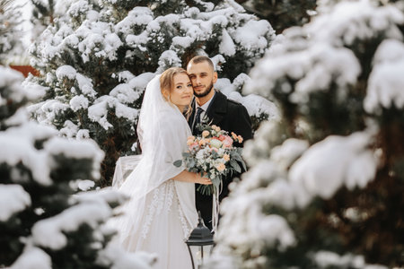 Portrait of the bride and groom between snowy trees. The groom hugs the bride in the winter park....