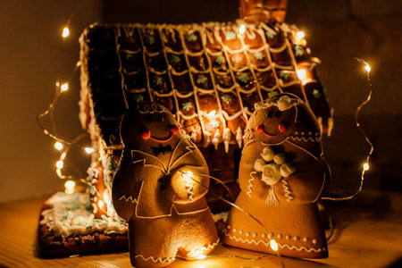 a gingerbread house in the role of a wedding cake decorated with a garland, gingerbread brides are...