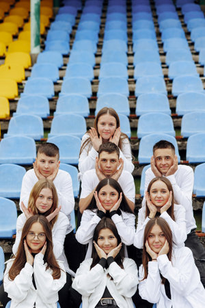 A group of many happy teenagers dressed in the same outfit having fun and posing in a stadium near a...