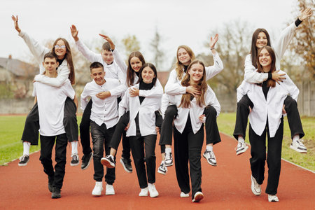 A group of many happy teenagers dressed in the same outfit having fun and posing in a stadium near a college. Concept of friendship, moments of happiness. School friendshipの写真素材