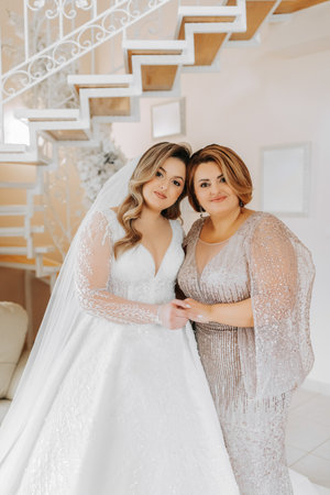 A beautiful and happy mother and her daughter, the bride, are standing next to each other. The best day for parents. Tender moments at the wedding.の写真素材