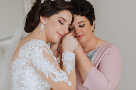 A beautiful and happy mother and her daughter, the bride, are standing next to each other. The best day for parents. Tender moments at the wedding.の写真素材