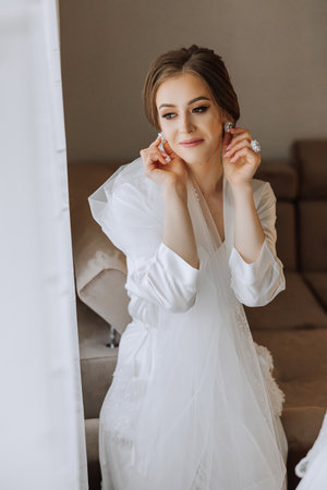 A beautiful brunette bride with a tiara in her hair is getting ready for the wedding in a beautiful robe in boudoir style. Close-up wedding portrait, photo.の写真素材