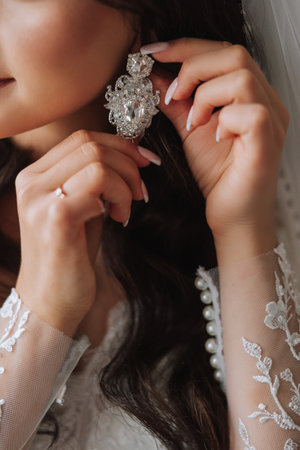 close-up of a beautiful girl in soft satin underwear wearing earrings. Wedding morning of the bride....