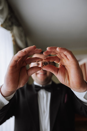 the groom holds the wedding rings with his fingers at the level of his eyes and looks into the...
