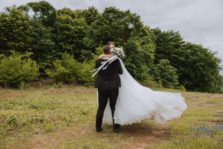 The bride in the arms of the groom. The groom is holding his bride in his arms and circling against the background of a beautiful park.の写真素材
