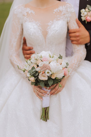 The groom hugs the bride from behind, the bride holds a wedding bouquet. Cropped photo. Groom in a black suit. Detailsの写真素材
