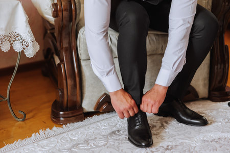 An elegant man wears black leather formal shoes. Tying shoes. Business man tying shoelaces on the floor. Up close The groom is preparing for the wedding.の写真素材