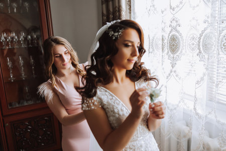 Morning of the bride. The bride's maid of honor helps the bride lace up her dress, fasten buttons on the dress or sleeves. Girlfriends help the bride fasten her dressの写真素材