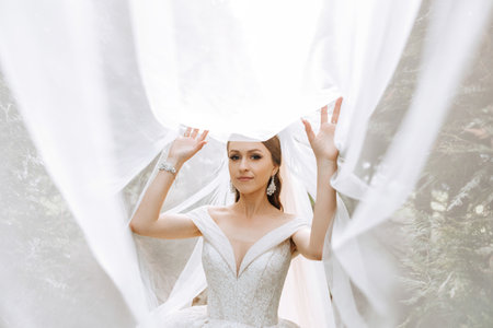 portrait of a beautiful young bride in a white dress with a long veil and a gorgeous hairstyle. Smiling bride. Wedding day. Gorgeous bride. Marriage.の写真素材