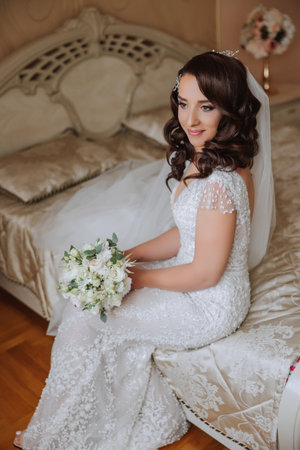A wonderful beautiful portrait of a young bride. Beautiful bride with wedding makeup and jewelry wreath on long curly hair. Wedding photo model with brown eyes in a beautiful interior.の写真素材