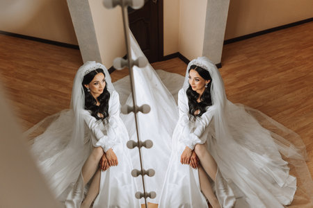 A beautiful bride is sitting in a dressing gown in the morning before the wedding ceremony in a hotel with a modern interior. Incredible hairstyle of the bride. Natural and modern makeup.の写真素材