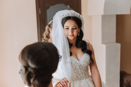 Wedding morning. Bridesmaids help put on the white wedding dress. A young woman is preparing to meet her groom and having fun with her friendsの写真素材