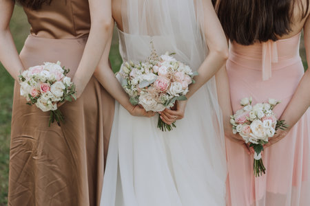 The bride and her two friends turned their backs to the camera, holding wedding bouquets of flowers behind their backs.の写真素材