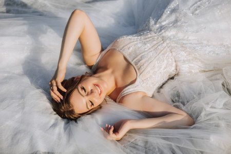 A beautiful bride in a white dress is lying. A girl in a white dress is resting. Beautiful hair and makeup. The model poses for the photographer.の写真素材