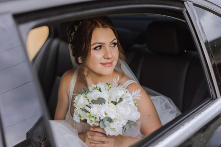 The bride looks out of the car window. Close-up portrait of a pretty shy bride in a car window. Bride smile emotionsの写真素材