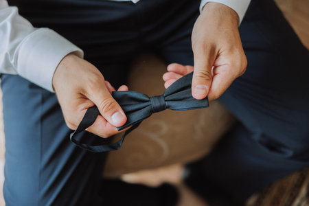 A bearded man in a white shirt adjusts his bow tie. Groom's morning. Close-up detail, men's tie for a wedding or an important meeting.の写真素材