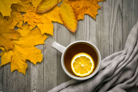 A mug of tea with lemon on a wooden table and autumn leaves.の写真素材