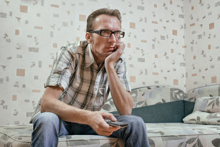 Sad and serious man with remote in his hand watch news broadcast on tvの写真素材