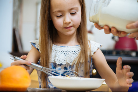 little  mothers helper. Small girl going to beat the dough for pancakes. Mom teach daughter to cookの写真素材