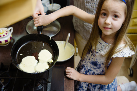 Little  mothers helper. Small girl making pancakes. Mom teach daughter to cookの写真素材
