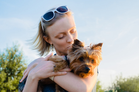 Beautiful young happy woman with blonde hair kissing small dogの写真素材