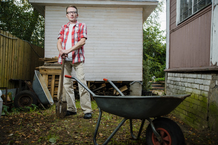 confident 30-40 years old farmer stand on his back yard and lean on the spade handleの写真素材