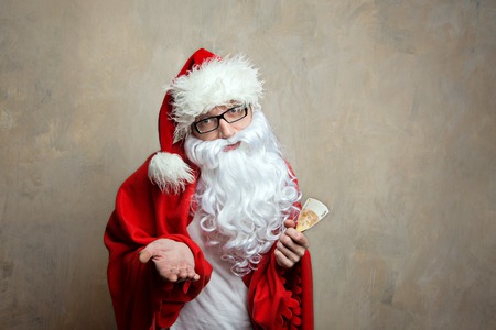 santa in home cloth and a euro banknote at the hand ask moneyの写真素材