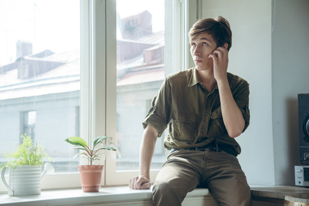 man in despair sitting on the windowsill makes gestureの写真素材