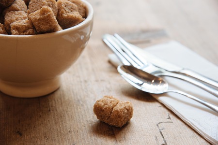 Bowl with brown sugar and small sugar piece on the wooden table with silverwearの写真素材