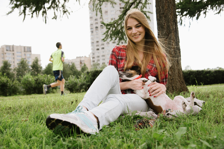 young pretty girl in red tartan shirt sit at the lawn and embrace her dog.の写真素材