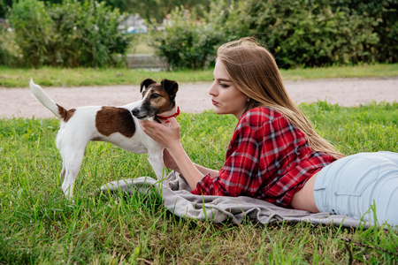Smile pretty 20-25 years girl in tartan red shirt with long hair lies on the grass with her active foxterrier. side viewの写真素材