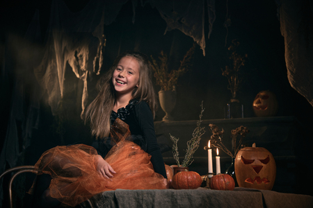 small girl in witch costume sit on the table in halloween decorationsの写真素材