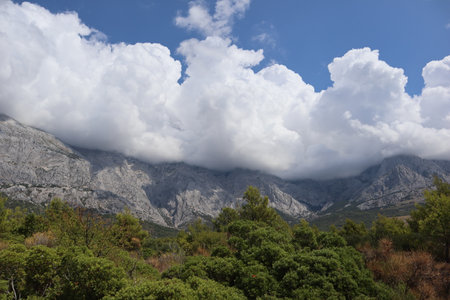 Cloudy landscape rocky mountain peaks are hidden behind large white clouds against a bright blue skyの写真素材